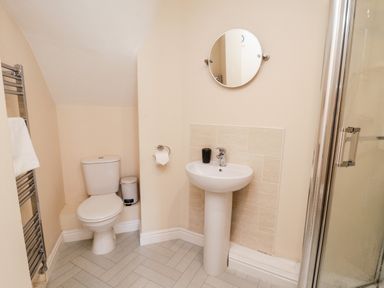 A bathroom with a toilet sink circular mirror and shower at Razorbill Cottage in Whitby