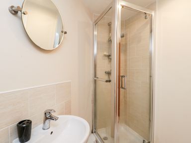 A bathroom with a round mirror above a sink and a glass door shower at Razorbill Cottage in Whitby