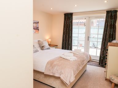 A bedroom with a bed with folded towels a bedside table with lamp curtains and glass doors at Razorbill Cottage in Whitby