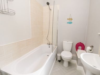 A bathroom with a bathtub and shower, a toilet, a sink, and wall decoration of two fish at Razorbill Cottage in Whitby