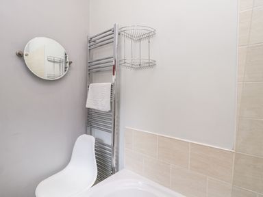 A bathroom corner with a white chair a round mirror a towel rack with a white towel and a metal corner shelf at Razorbill Cottage in Whitby