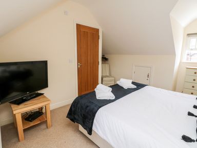 A bedroom with a bed, television on a wooden table, wooden door, striped chair, and chest of drawers at Razorbill Cottage Whitby