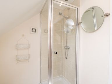 A shower enclosure with tiled walls a round mirror and a metal hanging storage rack at Razorbill Cottage in Whitby