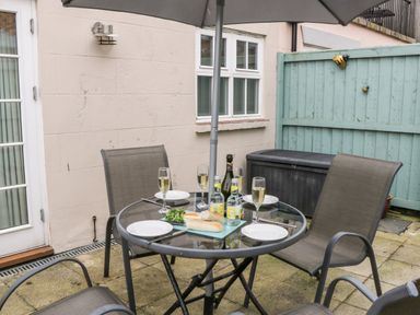 An outdoor patio with a glass table set with plates glasses and bottles surrounded by four chairs at Razorbill Cottage Whitby
