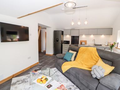 A living room with a gray sofa yellow blanket glass coffee table and a mounted television at Lands Brow Lodge in Wigton