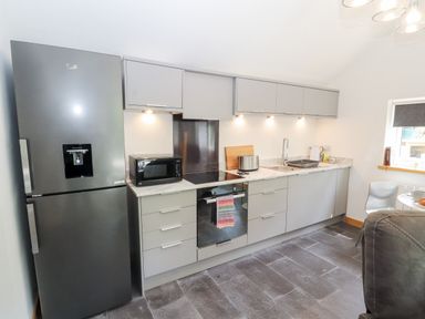 A kitchen with grey cabinets a black oven a black microwave a silver refrigerator and a sink at Lands Brow Lodge in Wigton
