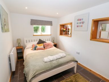 A bedroom with a bed with pillows and towels green throw rugs bedside lamps wall art and two recessed shelves at Lands Brow Lodge in Wigton