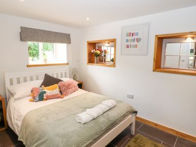 A bedroom with a bed covered with pillows and a blanket two windows and framed art on the wall at Lands Brow Lodge in Wigton