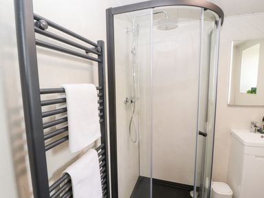 A bathroom with a glass shower enclosure a black towel radiator with white towels and a sink with mirror at Lands Brow Lodge in Wigton