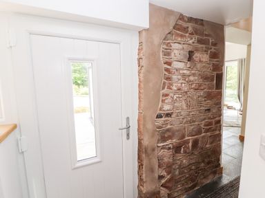 A white door with a rectangular window next to a partially exposed stone wall at Lands Brow Lodge in Wigton