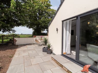 An outdoor patio with a table and chairs two potted plants and a glass sliding door leading inside at Lands Brow Lodge in Wigton