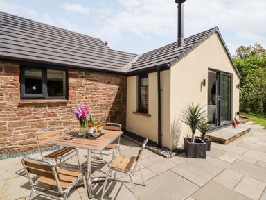 An outdoor patio area with a table and four chairs next to a stone and plaster house at Lands Brow Lodge in Wigton