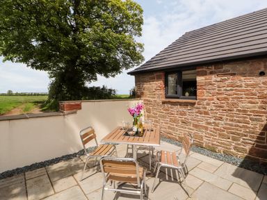 An outdoor patio with a wooden table and four chairs beside a stone building at Lands Brow Lodge in Wigton