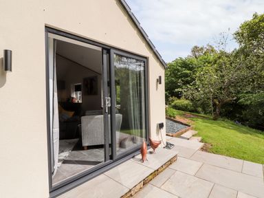 A patio with sliding glass doors leading into a living room and a garden with trees outside at Lands Brow Lodge in Wigton