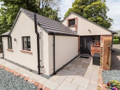 The exterior of a small house with cream walls black windows a black door and a stone tiled patio at Lands Brow Lodge in Wigton