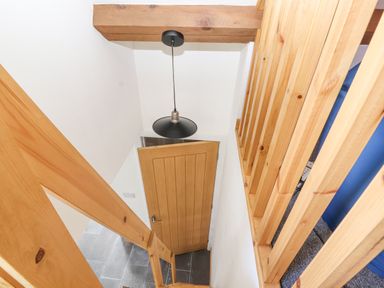 A staircase with wooden railings leading to a door with a pendant light hanging above at Lands Brow Lodge in Wigton