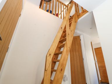 A wooden staircase with railing leading to an upper floor inside a hallway with wooden doors at Lands Brow Lodge in Wigton