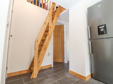 A wooden staircase next to a wooden door and a gray fridge in a room with tiled floor at Lands Brow Lodge in Wigton