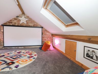 An attic room with a projector screen on a brick wall a round patterned rug pillows a skylight and a framed photo at Lands Brow Lodge in Wigton