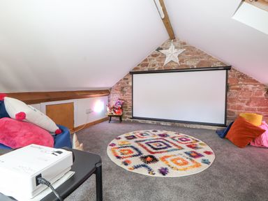 An attic room with a projector screen on a brick wall a colorful round rug cushions and a projector on a table at Lands Brow Lodge in Wigton