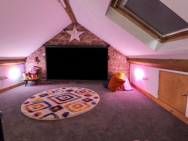 A cozy attic space with a colorful rug cushions a snack table and a screen on a stone wall at Lands Brow Lodge in Wigton
