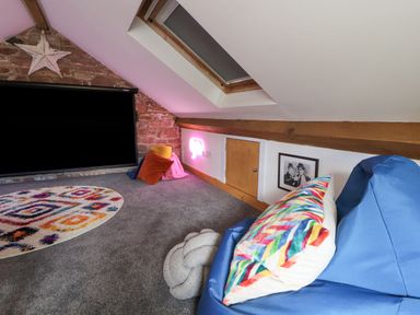 A loft room with a gray carpet colorful rug bean bags a small wooden door and a skylight window at Lands Brow Lodge in Wigton