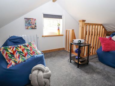 A loft space with blue bean bags a small black table with a projector and lamp and a window with a blind at Lands Brow Lodge in Wigton