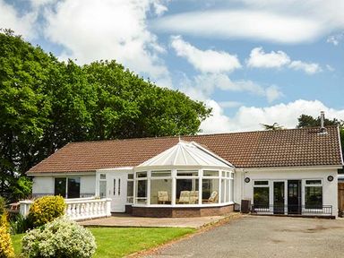 A single-story house with a tiled roof a white conservatory and a front garden with bushes at Treetops in Govilon near Abergavenny