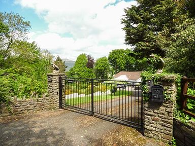 A gated entrance with stone pillars and iron gate leading to a driveway and house surrounded by trees at Treetops in Govilon near Abergavenny