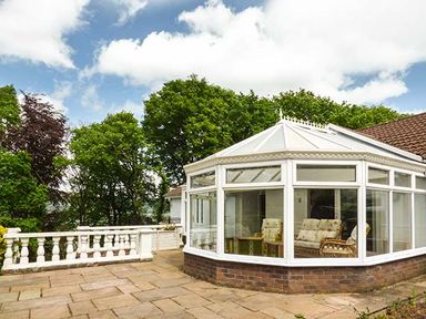 A conservatory with chairs and a table surrounded by a stone patio and trees at Treetops in Govilon near Abergavenny