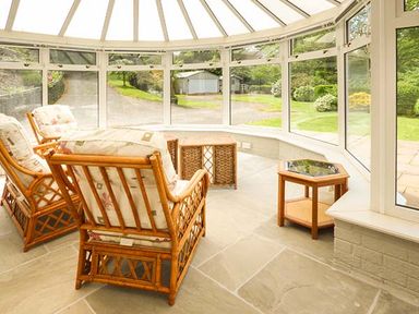 A conservatory with wicker chairs and tables overlooking a garden at Treetops in Govilon near Abergavenny