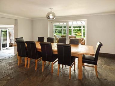 A dining room with a wooden table and eight black chairs and glass doors leading to a garden at Treetops in Govilon near Abergavenny