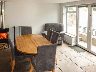 A dining room with a wooden table and gray chairs near a stove and armchair by glass doors at Treetops in Govilon near Abergavenny
