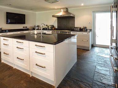 A kitchen with white cabinets a black countertop a stove a mounted television and a door to outside at Treetops Govilon near Abergavenny