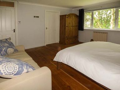A bedroom with a bed a sofa with cushions a wooden wardrobe and a window at Treetops in Govilon near Abergavenny
