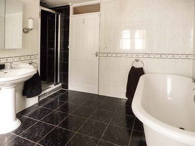A bathroom with a pedestal sink a bathtub a shower enclosure and black towels at Treetops in Govilon near Abergavenny