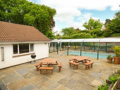 An outdoor patio area with two wooden picnic tables a covered swimming pool and a small white building at Treetops in Govilon near Abergavenny