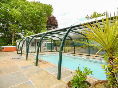 A covered outdoor swimming pool with a hot tub and plants around at Treetops in Govilon near Abergavenny