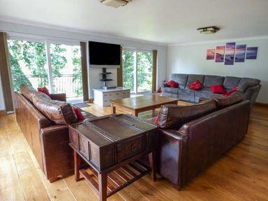 A living room with leather and fabric sofas a wooden coffee table a TV mounted on the wall and large windows at Treetops in Govilon near Abergavenny