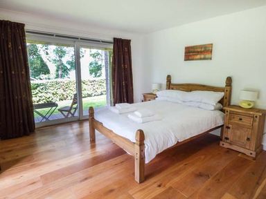 A bedroom with a double bed between two wooden bedside tables and sliding glass doors opening to a garden at Treetops in Govilon near Abergavenny