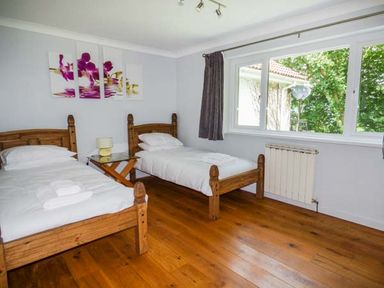 A bedroom with two single wooden beds a small table and a window with curtains at Treetops Govilon near Abergavenny