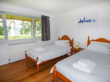 A bedroom with two single beds a wooden nightstand and a window with a view at Treetops in Govilon near Abergavenny