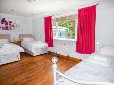 A bedroom with three single beds red curtains and wooden floor at Treetops in Govilon near Abergavenny