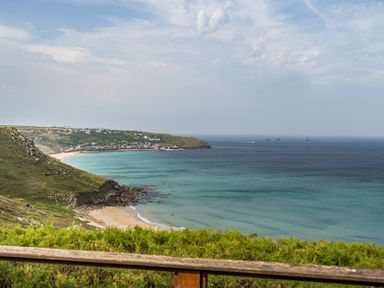 A view of a beach and sea with cliffs and houses at Cragford in Sennen Cove