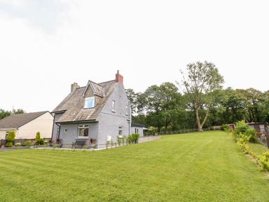 A house with a large grassy yard and trees in the background at Pondfield Gate in Cwmgors