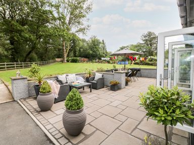 A patio with outdoor seating and tables surrounded by plants and a lawn with trees at Pondfield Gate in Cwmgors