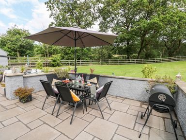 An outdoor patio area with a dining table and chairs under an umbrella and a barbecue grill at Pondfield Gate in Cwmgors
