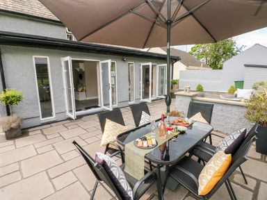 A patio with a glass table and chairs under an umbrella next to a house with open doors at Pondfield Gate in Cwmgors