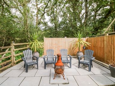 An outdoor patio area with four plastic chairs a small fire pit and potted plants at Pondfield Gate in Cwmgors