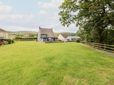 A large grassy yard with a grey house and a smaller white building surrounded by trees and hills at Pondfield Gate in Cwmgors